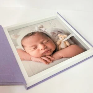 1. Foto de bebê recém-nascido em quadro de vidro com fundo branco e detalhe em lilás.