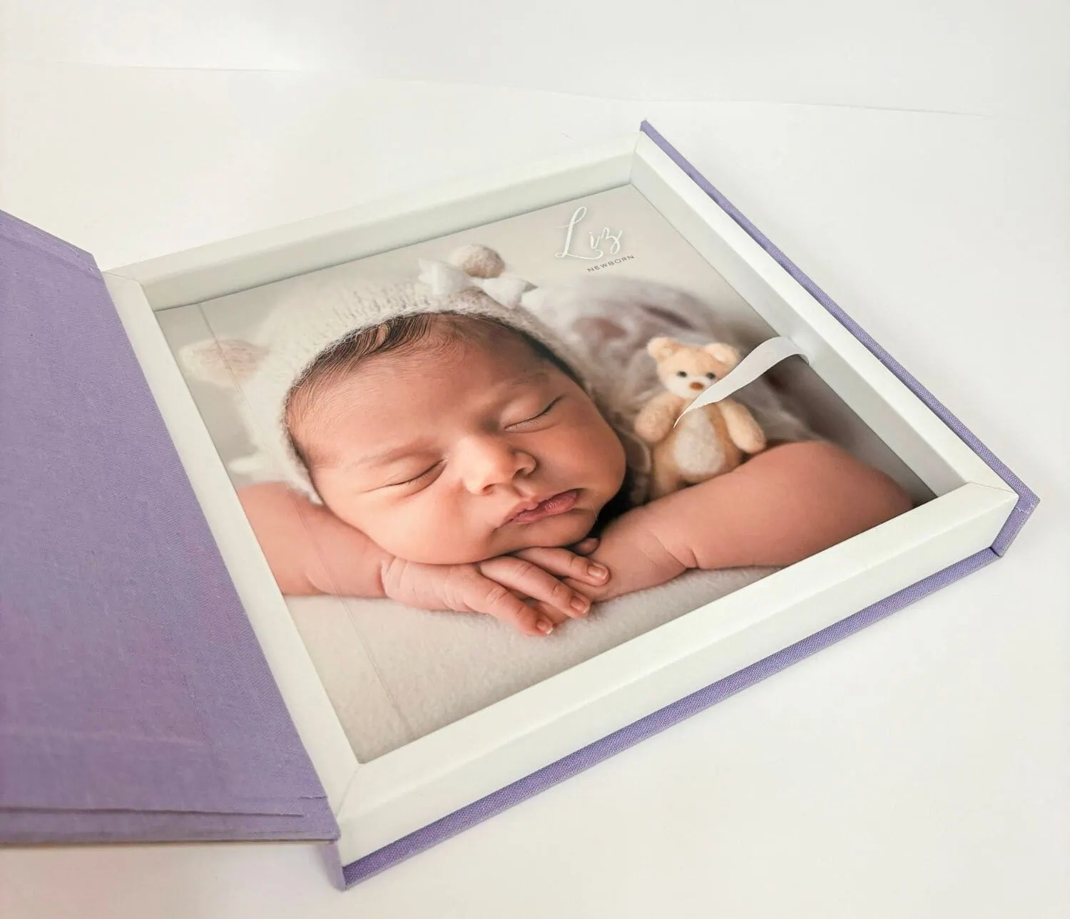1. Foto de bebê recém-nascido em quadro de vidro com fundo branco e detalhe em lilás.